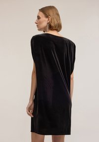 Schwarzes Samtkleid mit lockerem Schnitt und kurzen Ärmeln. Es verfügt über einen runden Ausschnitt und einen sanft drapierten Rücken, der eine glatte Textur bietet.