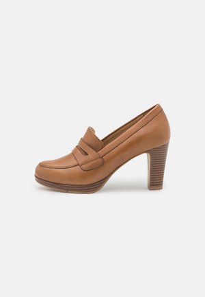 Brown leather high-heeled loafers with a rounded toe, featuring twin leather straps and a stacked wooden heel with a textured finish.