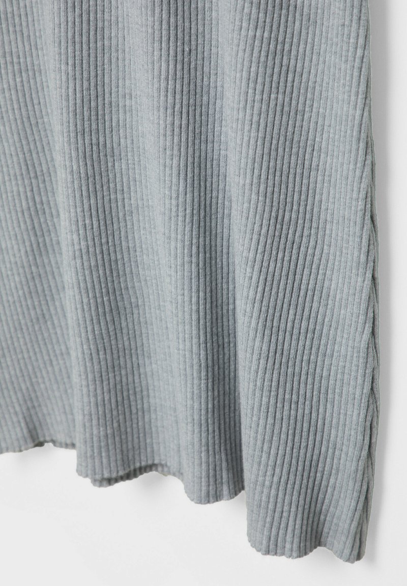 Textil de ribetes grises con rayas verticales, textura suave y dobladillo curvado. Los lados presentan un detalle de costura decorativa.