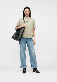 Tricou din bumbac bej cu un logo negru, asortat cu blugi largi, decolorati, de culoare bleu deschis și cizme negre cu toc. Geantă de umăr neagră inclusă.