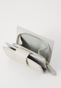 Lys grå lommebok med steinaktig tekstur, glidelås, flere kortlommer og en glatt indre foring. Kompakt design med klafffeste.