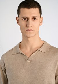 Beige stickad polo med V-ringning och klassisk krage, med en mjuk yta och subtila ribbade detaljer.