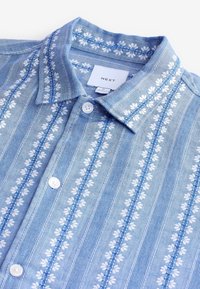 Chemise bleu clair avec des rayures verticales florales blanches, boutons blancs et col, taille medium de la marque NEXT.