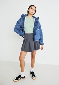 Veste en denim avec doublure en fourrure, haut côtelé vert, jupe plissée grise, baskets noir et blanc avec des chaussettes rayées roses.