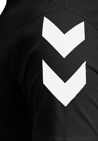 Czarna koszulka z dużym białym wzorem chevron na prawym ramieniu. Wykonana z bawełny o gładkiej fakturze, krótki rękaw.