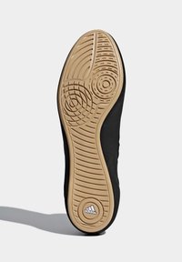 Black sneaker sole with a textured, gum rubber outsole featuring circular and linear patterns, branded with a silver adidas logo.