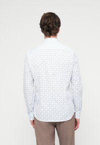 Λευκό πουκάμισο με μακριά μανίκια και μικρό μπλε λουλουδάτο μοτίβο. Διαθέτει κλασικό γιακά και στρογγυλεμένη άκρη· κατασκευασμένο από ελαφρύ ύφασμα.