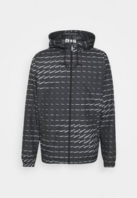 Černá zipová bunda s kapucí, která má opakující se bílý vzor loga. Lehký materiál, elastické manžety a nastavitelné šňůrky.