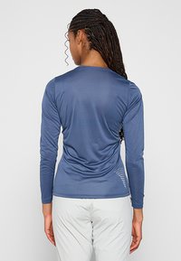 Długi rękaw sportowa koszulka w kolorze niebieskim, wykonana z gładkiego, oddychającego materiału. Posiada teksturowany wzór i odblaskowe akcenty na plecach.