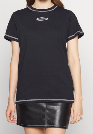 Donna che indossa una T-shirt nera a maniche corte con cuciture bianche e logo Ellesse abbinata a una minigonna nera in pelle.