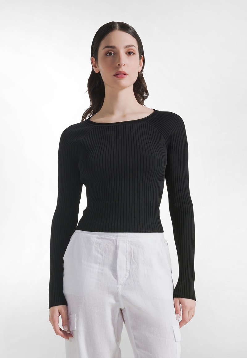 Schwarzes, geripptes Langarmshirt mit rundem Ausschnitt, schmal geschnitten und mit glatter Textur, kombiniert mit weißen, strukturierten Hosen.