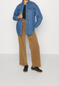 Quiltad blå denimskjorta med två bröstfickor, kombinerad med tanfärgade vida byxor och svarta sneakers med gummisulor.