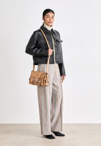 Black leather jacket with a cropped silhouette, paired with striped wide-leg pants. A tan crossbody bag features silver hardware and accents.