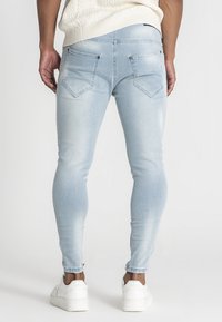 Svetlo modré skinny džínsy s vyblednutou textúrou, s dvoma zadnými vreckami, jemným prešívaním a obnošenými lemy, skombinované s bielymi teniskami.
