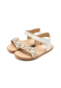 Sandalias blancas con una correa de acento trenzada en oro y una suela plana de color marrón. El diseño presenta una correa para el tobillo con un cierre de gancho y bucle.