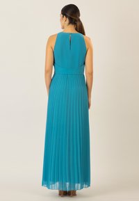 Teal maxi dress with pleats, featuring a high neckline, open back detailing, and a fitted waist. Crafted from lightweight, flowing fabric.