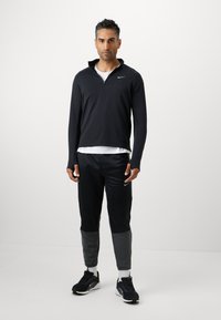 Crni sportski zip-up jakna od teksturiranog materijala, u kombinaciji s crnim trenirkom sivoj naglascima. Crne sportske cipele dopunjuju ovaj outfit.