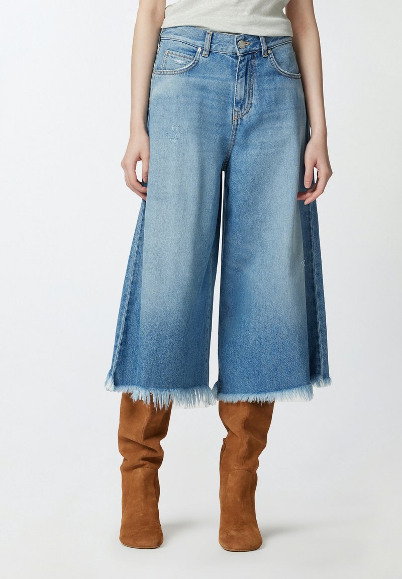 Světle modré denimové culottes s roztrhaným lemem, vysokým pasem a širokými nohavicemi. V páru s béžovými semišovými kozačkami po kolena.