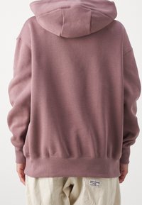 Sudadera con capucha de gran tamaño, hecha de una tela suave en color malva, con puños y dobladillo acanalados, que presenta un diseño simple y sin gráficos visibles.