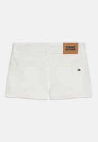Vita denimshorts med en brun läderlapp som har texten "TOMMY HILFIGER", två bakfickor och subtila sömnadsdetaljer.