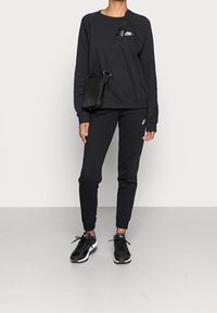 Svart Nike sweatshirt med rundad halsringning, matchande svarta joggers. Svarta träningsskor och en liten svart axelväska fulländar looken.