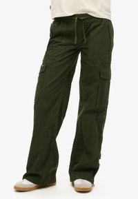 Pantalons cargo en mélange de coton vert foncé. Coupe décontractée avec taille élastique et cordon de serrage ajustable. Comprend de nombreuses poches et des détails zippés.