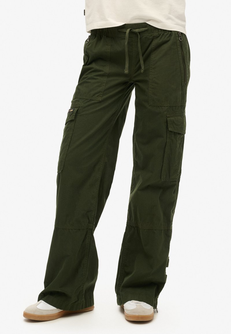 Pantalons cargo en mélange de coton vert foncé. Coupe décontractée avec taille élastique et cordon de serrage ajustable. Comprend de nombreuses poches et des détails zippés.