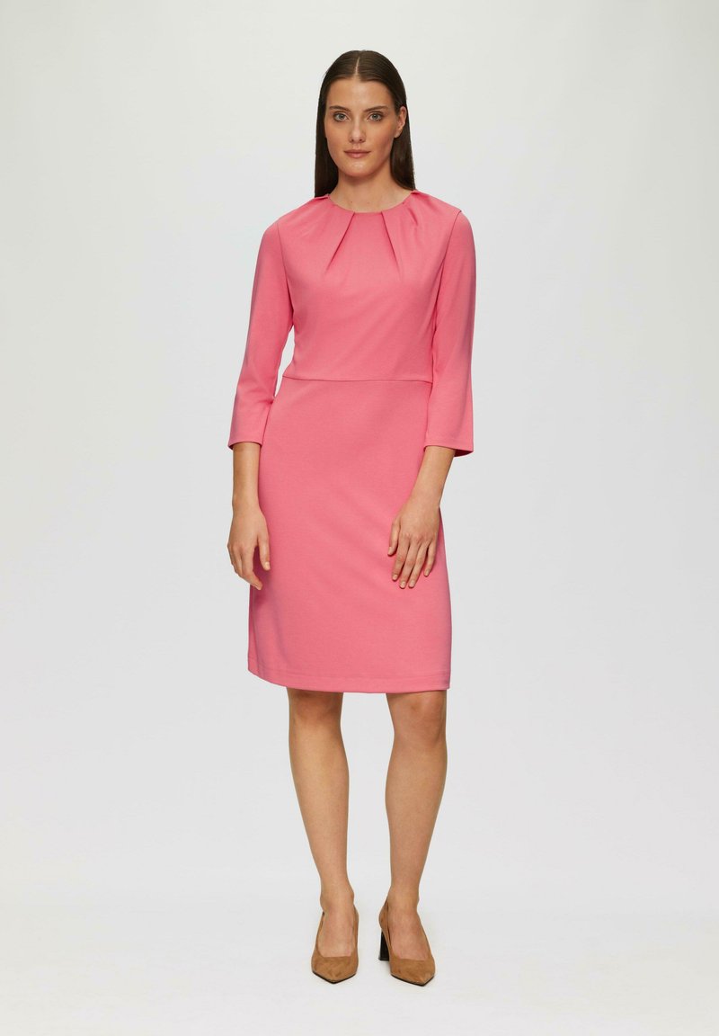 Ein knielanges, pinkes Kleid aus glattem Stoff, das über drei Viertelärmel verfügt und subtile Falten am Ausschnitt aufweist.