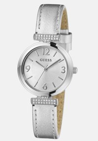 Hõbedane kell ümmarguse näo, tekstureeritud kelladraami ja metallnumbritega. Omab hõbedast nahkrihma ja rhinestone'idega kaunistatud aksenti.