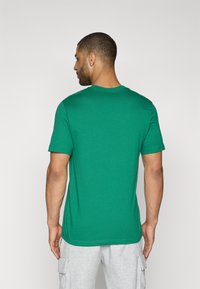 Zielony bawełniany T-shirt z krótkim rękawem i okrągłym dekoltem, o gładkiej teksturze. Widok z tyłu pokazuje prosty krój i minimalistyczny design.