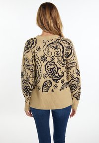 Beżowy sweter z czarnym wzorem paisley, ribbowym dołem i mankietami oraz okrągłym dekoltem. Materiał wydaje się miękki i ma luźny krój.