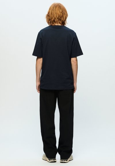 Marineblå bomulds T-shirt med korte ærmer, rund halsudskæring og afslappet pasform, kombineret med løse sorte bukser og lyse sneakers.