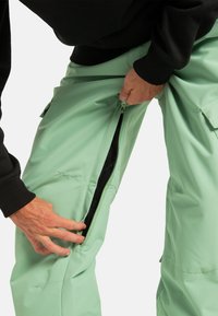 Miętowe spodnie cargo o dopasowanym kroju, z kieszeniami cargo i bocznymi suwakami, wykonane z gładkiego, lekkiego materiału. Czarne akcenty na pasku.