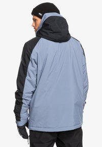 Helleblaue und schwarze gepolsterte Jacke mit Kapuze, die kontrastierende Einsätze, eine glatte Textur und verstellbare Bündchen aufweist.