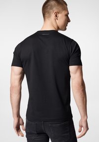 Czarny t-shirt z krótkim rękawem, wykonany z gładkiego materiału, z okrągłym dekoltem i subtelnym logo marki na plecach blisko dekoltu.