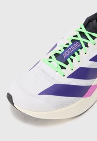 Fehér sportcipő lila és rózsaszín kiegészítőkkel. Hálós felsőrész, zöld fűzők, és elegáns, áramvonalas dizájn jellemzi. Az 'ADIZERO' márkanevének feltüntetése.