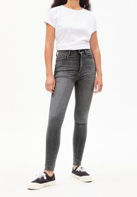 Jeans de denim gris de alta cintura con corte ajustado, con pasadores para cinturón y cinco bolsillos, combinados con una camiseta blanca básica y zapatillas negras.