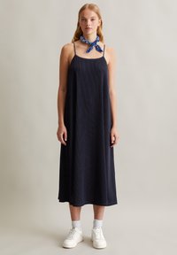Marineblaues, geripptes Midikleid mit dünnen Trägern, das eine fließende Silhouette bietet. Kombiniert mit einem blauen, gemusterten Schal und weißen Sneakers.