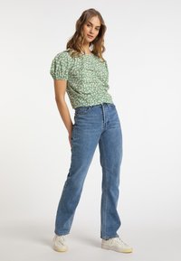Grünes Blumendruck-Top mit kurzen Ärmeln und gerafften Details, kombiniert mit hochgeschnittenen blauen geraden Jeans und weißen Sneakern.
