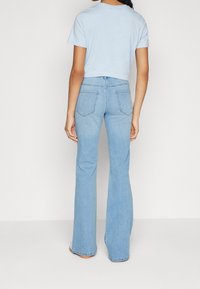 Vaaleansininen lyhythihainen cropped t-paita yhdistettynä korkeavyötäröisiin vaaleansinisistä farkuista valmistettuihin leveälahkeisiin housuihin, joissa on viisi taskua ja hienovaraiset ompeluyksityiskohdat.