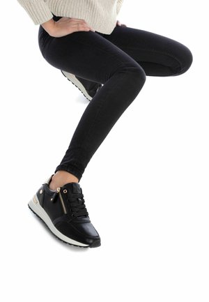 Zapatillas negras con parte superior de cuero, suela blanca y detalle de cremallera dorada. Combinadas con jeans skinny negros y un suéter de un color claro.
