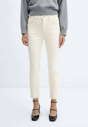 Jeans de color crema con corte ajustado, diseño de cinco bolsillos y cintura de altura media, combinados con tacones altos de tiras negras y un suéter gris.