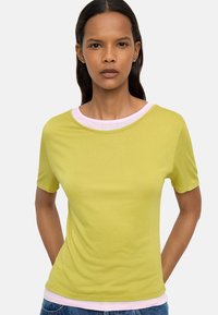 Limonkowa koszulka z krótkim rękawem z różowym okrągłym dekoltem. Tkanina wydaje się gładka i elastyczna, z dopasowanym krojem.