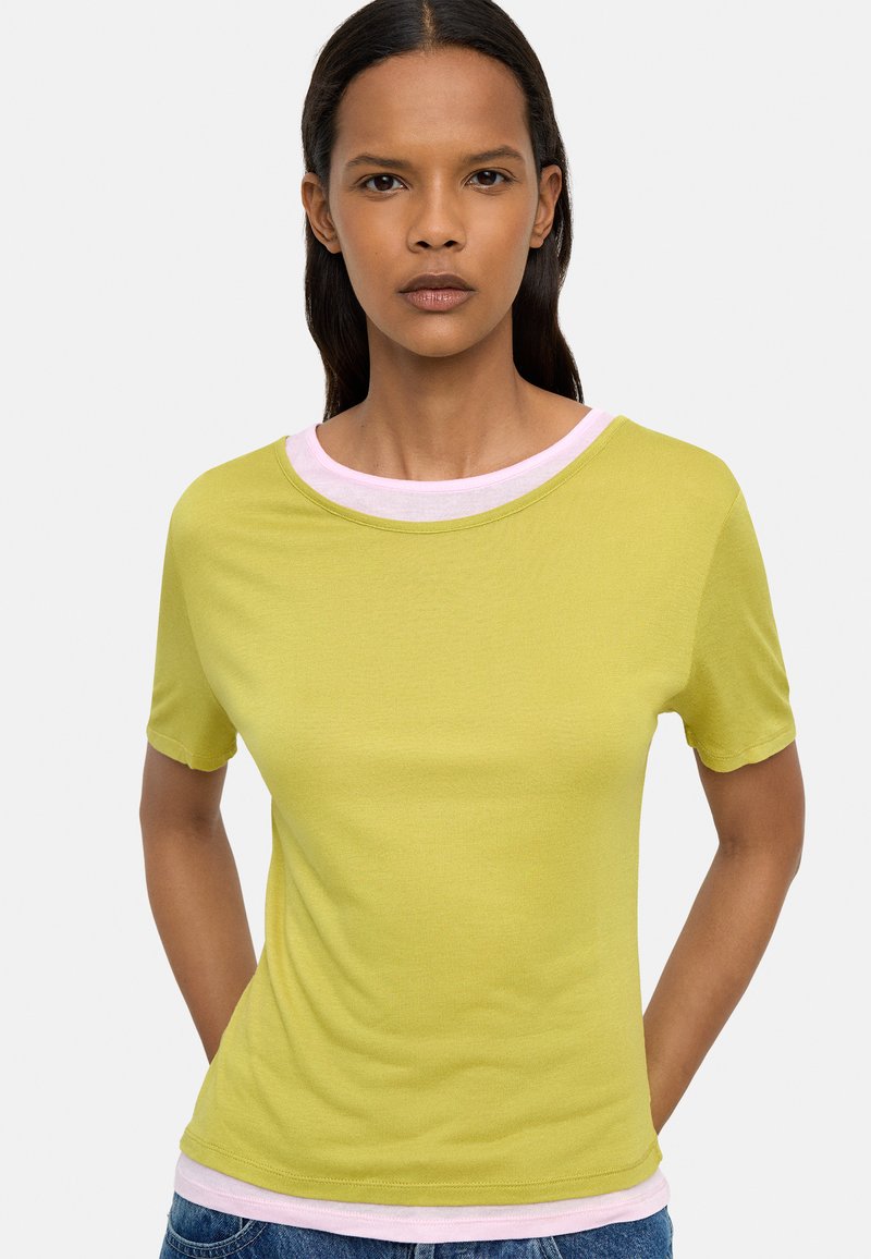 Limonkowa koszulka z krótkim rękawem z różowym okrągłym dekoltem. Tkanina wydaje się gładka i elastyczna, z dopasowanym krojem.