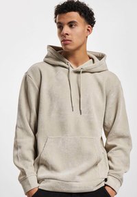 Beige ribbet hettegenser med frontlomme, justerbare snorer og en myk tekstur. Designet med en avslappet passform og lange ermer.