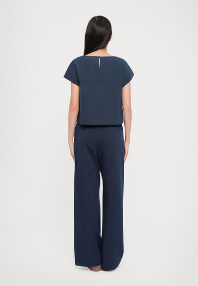 Haut bleu marine à manches courtes avec un design court et un détail en trou de serrure dans le dos, associé à un pantalon large bleu marine, tous deux en tissu lisse.