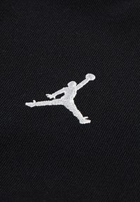 Black fabric with a textured surface featuring a white embroidered silhouette of a person leaping while holding a basketball.