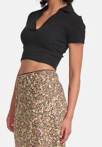 Černý, krátký rukáv, brýle crop top s výstřihem do V. V páru s sukní s květinovým vzorem, která má malé, multikolorové květy na tmavém pozadí.