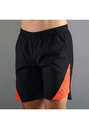 Hombre con pantalones cortos deportivos negros con cintura elástica y paneles laterales naranjas etiquetados con "ENDLESS" sobre un fondo neutro.