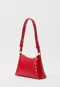 Rote Lederhandtasche mit goldenen Nieten, dreieckigen und sternförmigen Akzenten. Verfügt über einen Reißverschluss und eine strukturierte Form mit einem abnehmbaren Tragegurt.